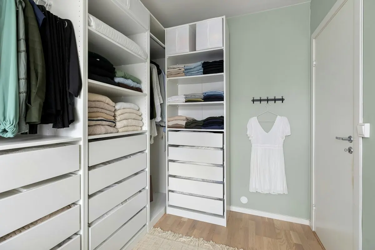 A bright walk-in closet with neatly folded clothes and white drawers